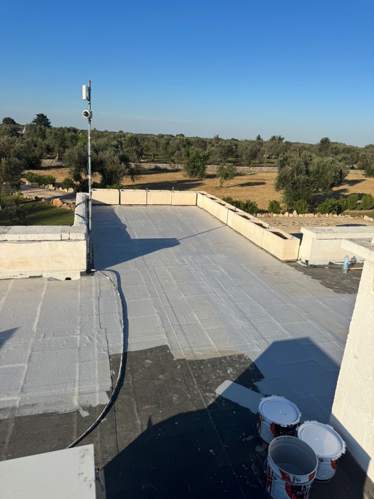 Flat roof coating application in progress — coating buckets and part-coated surface